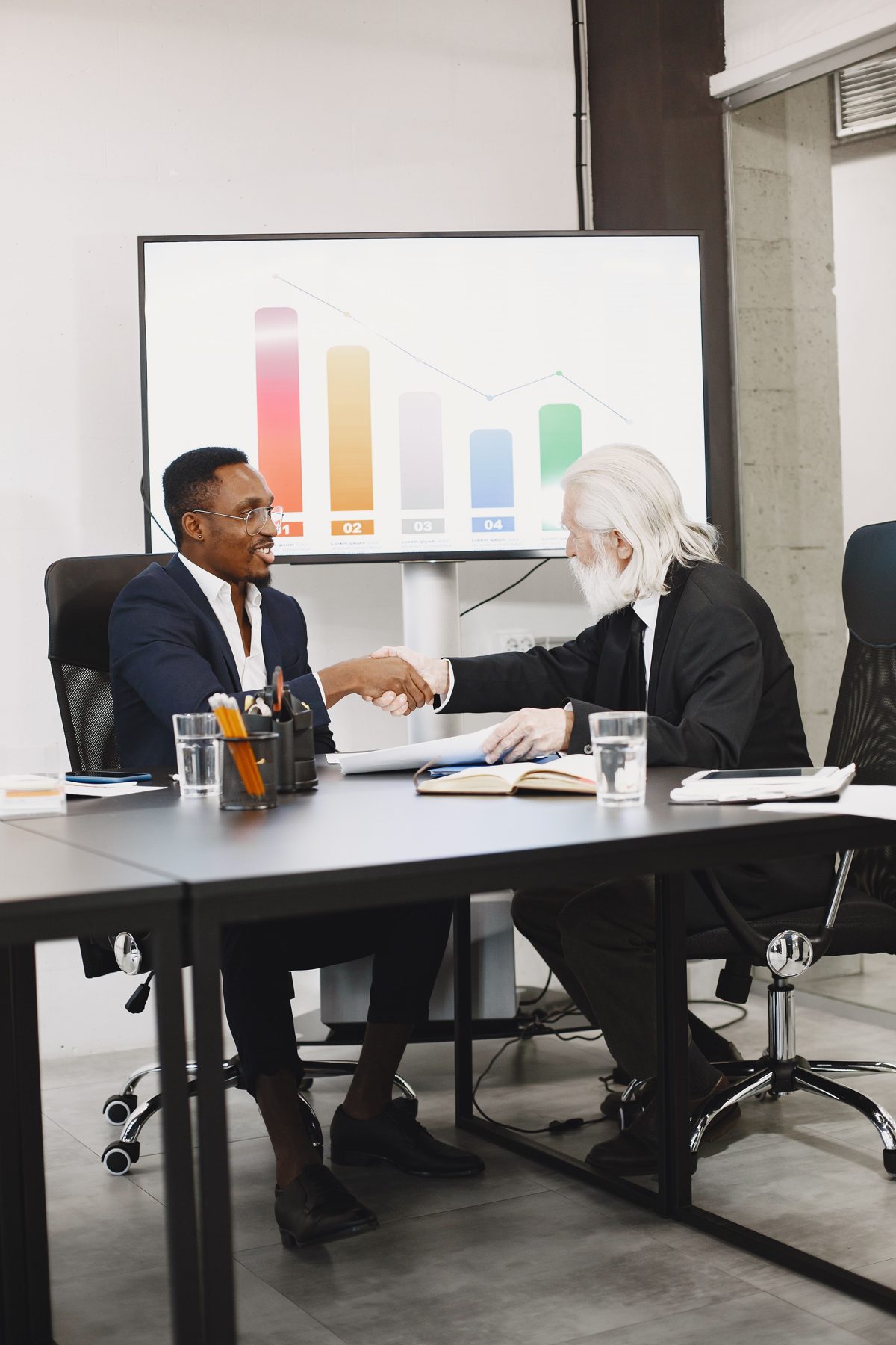 Two advisers shaking hands in front of a screen showing a chart